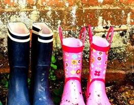 Two pairs of wellington boots, one dark blue with black and white striped detail, the other pink with red and yellow flowers.